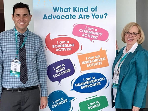 Carol Dow-Richards is posing with her son, David, next to a promotional banner