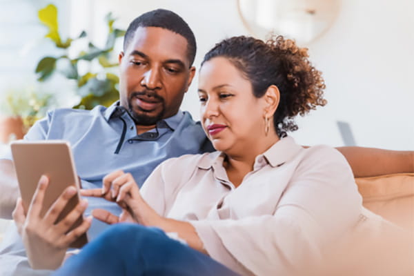 A man and woman sitting on a sofa are interacting with a touchscreen device.