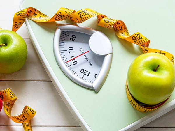 Manzanas verdes y una cinta métrica colocadas sobre una báscula.