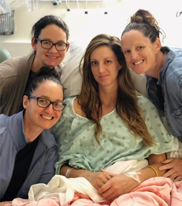 Kaitlyn Fieseler, sobreviviente de un ataque o derrame cerebral, está sentada en una cama de hospital rodeada de sus hermanas