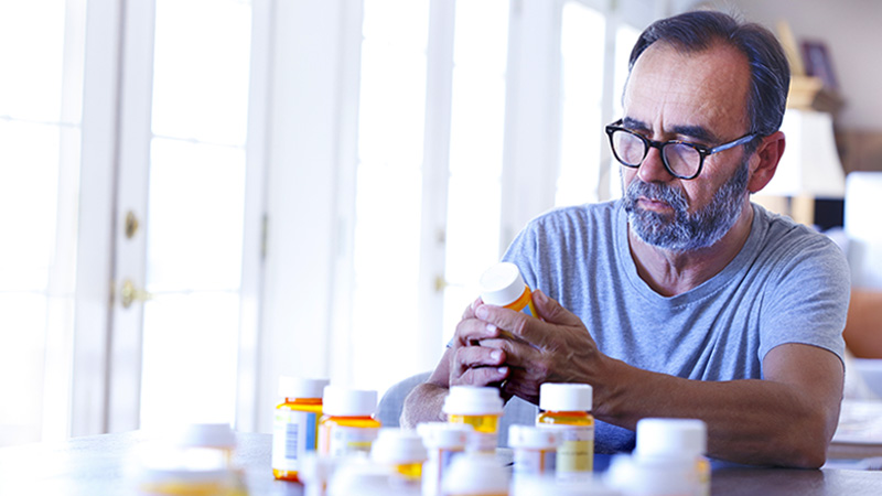 Un hombre de origen latino de edad avanzada está sentado y ordena unos medicamentos con receta en una mesa.