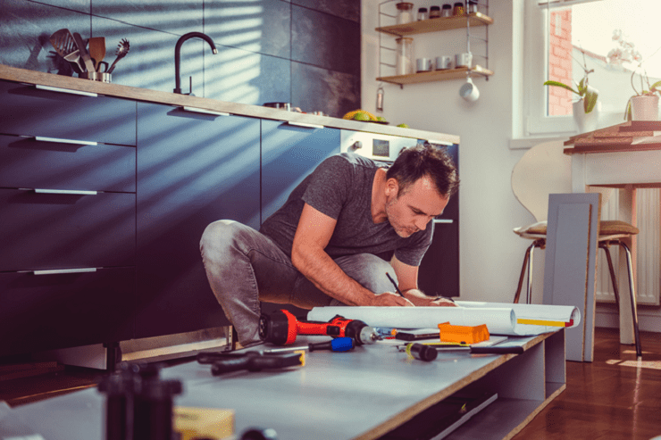 Un hombre vestido de manera casual está construyendo un mueble en una cocina.